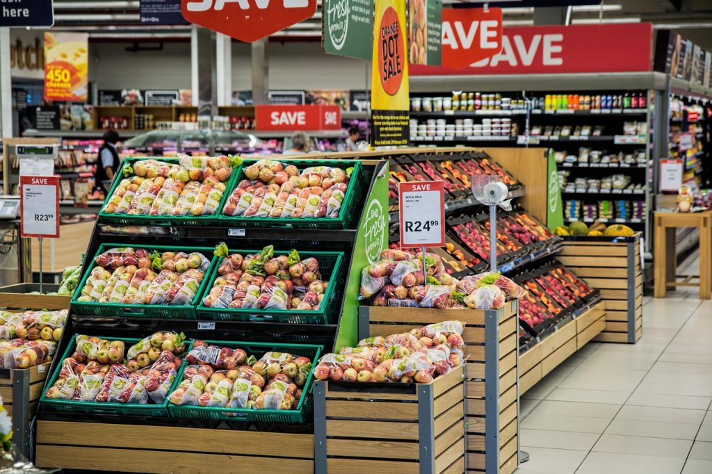 Supermarket aisle with fresh apples and produce on display, featuring discount signs and neatly arranged shelves
