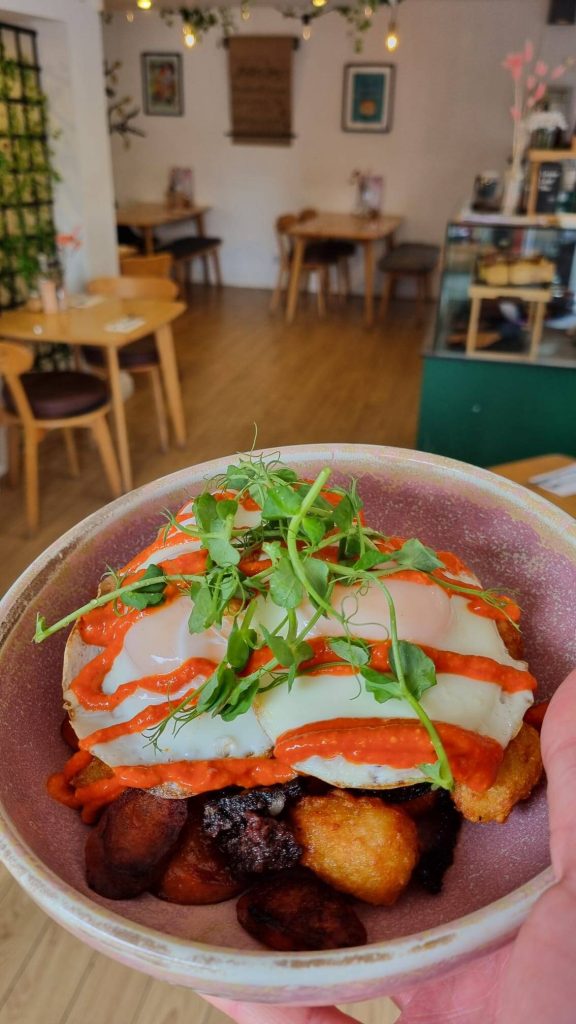 Delicious brunch dish topped with poached eggs, vibrant red sauce, and fresh greens in a cosy café setting