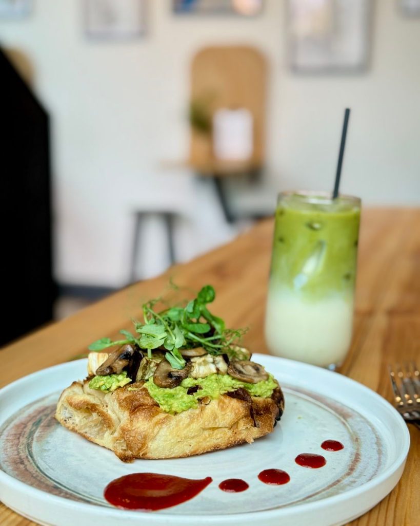 Delicious sourdough toast with avocado, mushrooms, and greens served with a refreshing iced matcha latte in a café setting