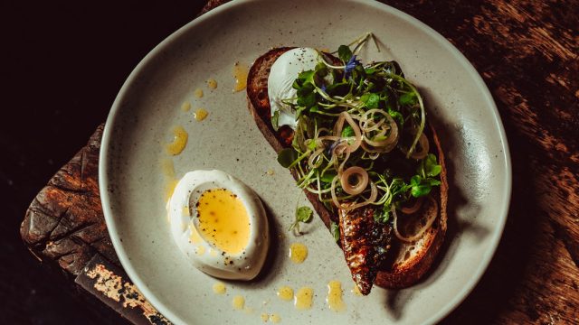 Gourmet plate with soft-boiled egg, toast topped with greens and shallots, drizzled with dressing, on rustic table