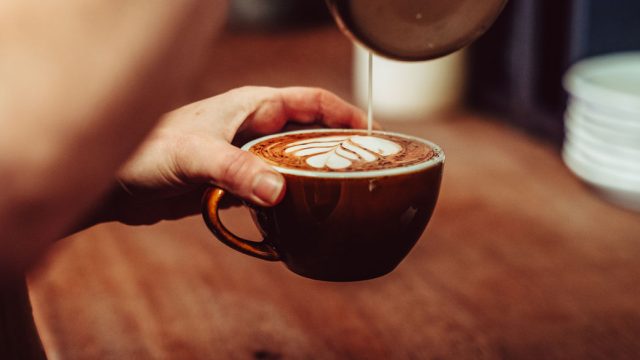 Barista crafting latte art in a brown cup with steamed milk and espresso on a wooden table