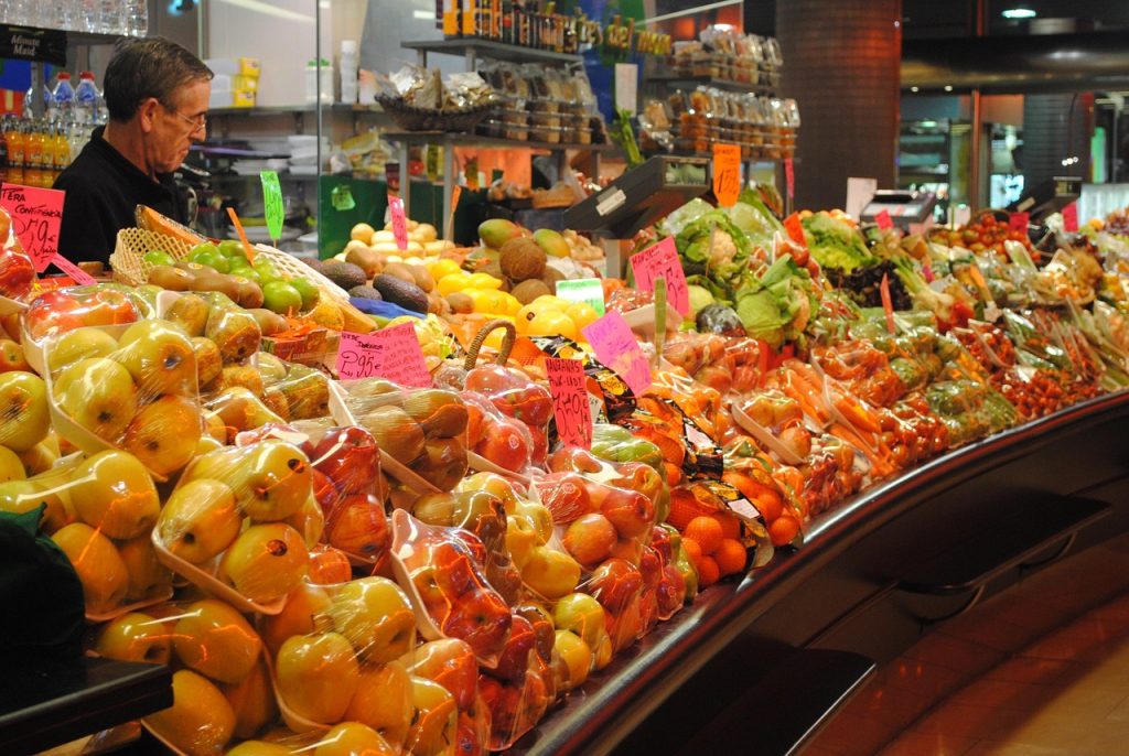 Fruit and vegetable market stall with vibrant produce and vendor in a busy indoor setting