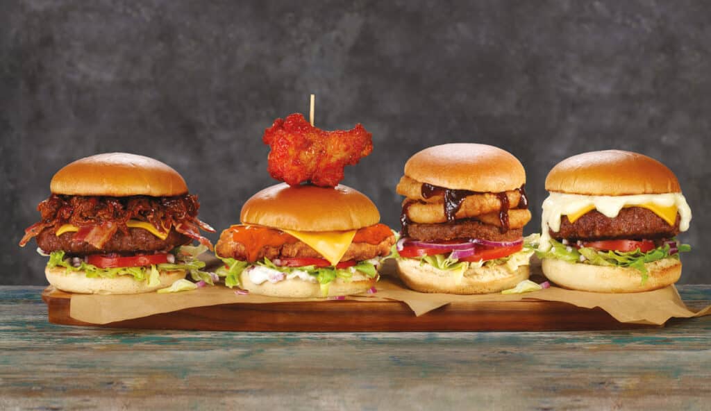 Four gourmet burgers with diverse toppings on a wooden board against a rustic background