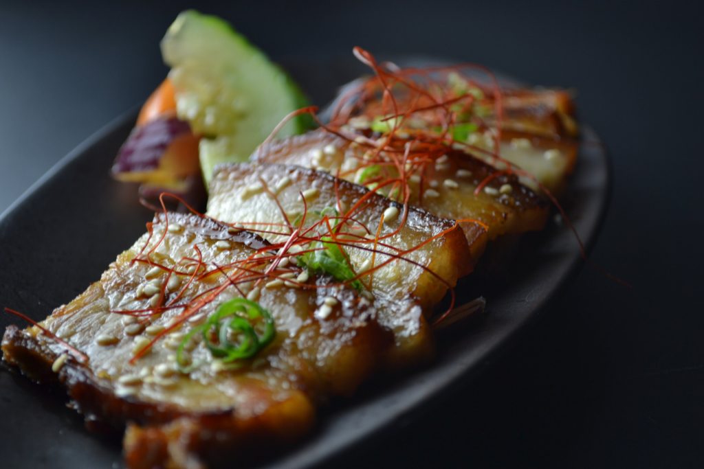Grilled fish with sesame seeds and thin red peppers garnished with cucumber on a black plate