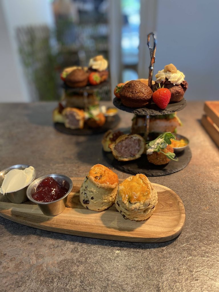 Afternoon tea with scones, clotted cream, jam, and a tiered stand of desserts and savoury bites on a wooden board