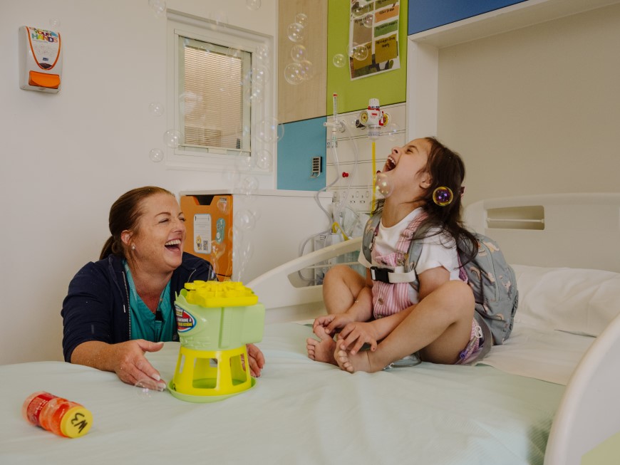 Child and medical staff laughing and playing with bubbles in a hospital room