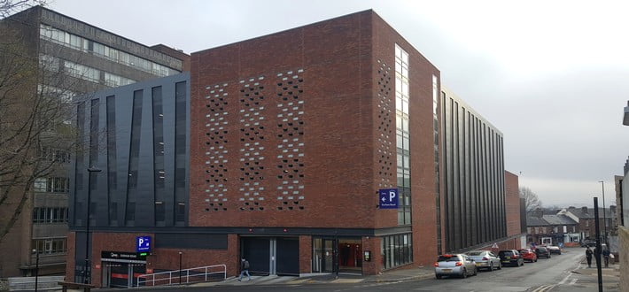 Modern multi-storey car park in urban setting with brick and grey cladding, overcast sky in background