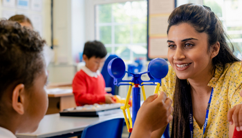 Teacher engaging a pupil in a classroom science activity with balancing scales