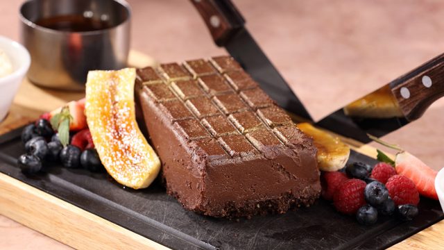 Decadent chocolate dessert with fresh berries and caramelised banana on a serving board being sliced by knife