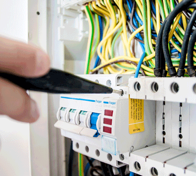 Electrician adjusting circuit breakers in a well-organised electrical panel with colourful wires