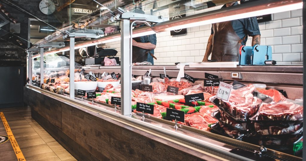 Butcher shop meat display with various cuts, price tags, and trays showcasing fresh products in a clean, well-lit setting